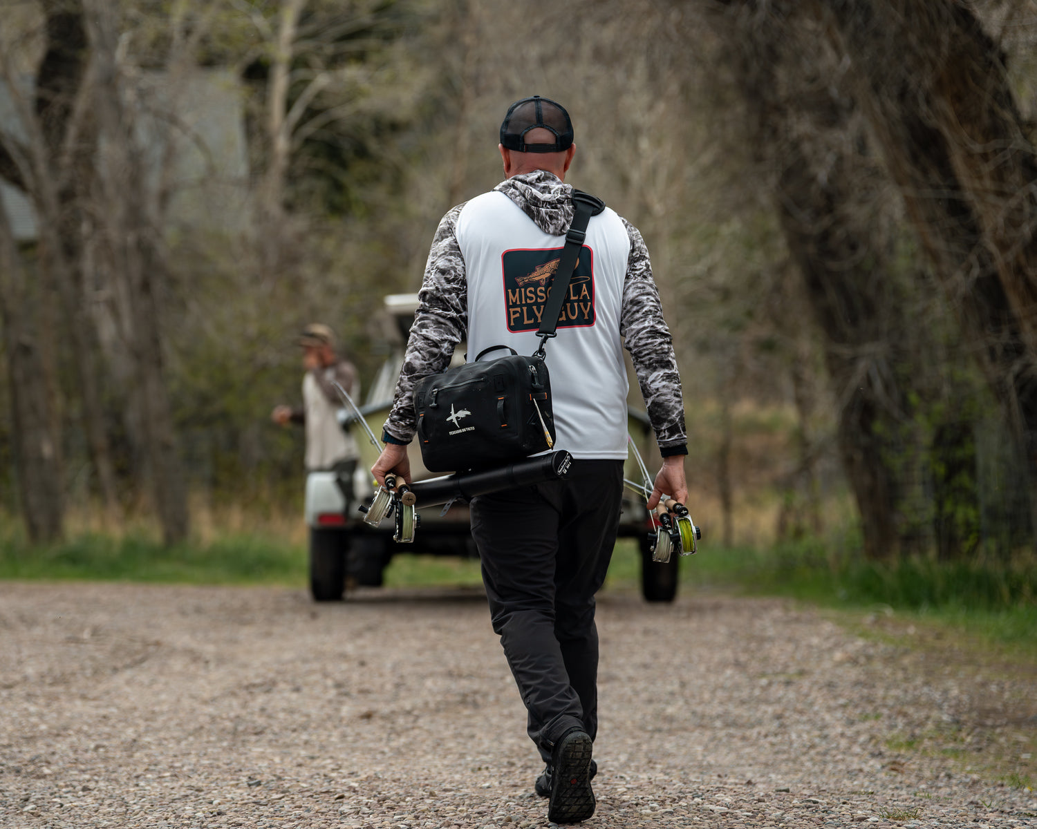 An angler carrying fly rods and a waterproof hip pack on the Missouri River