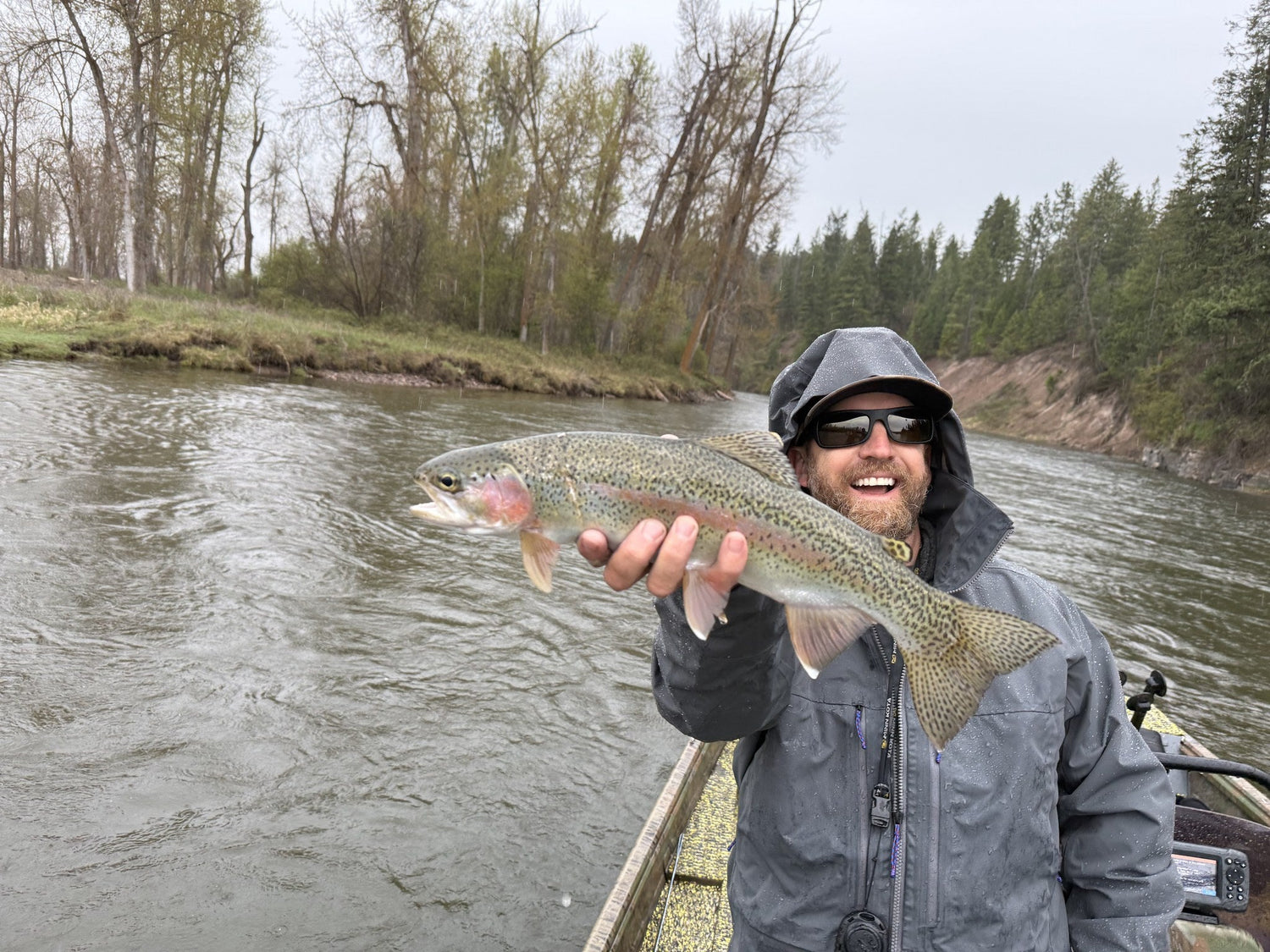 Angler in rain gear holding a rainbow trout on the Clark Fork, Montana