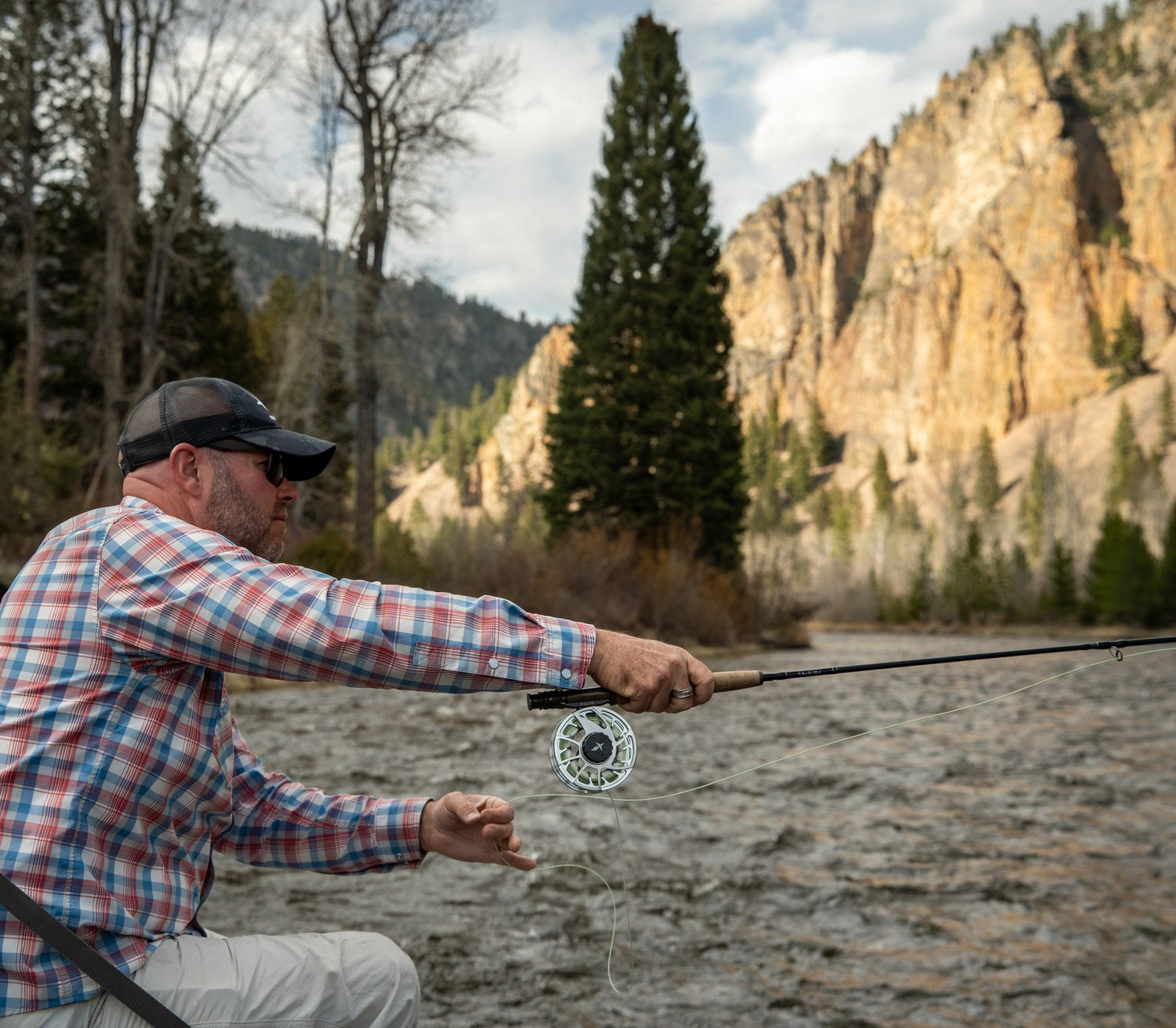 Angler fly casting on Rock Creek with a canyon cliff behind, Montana