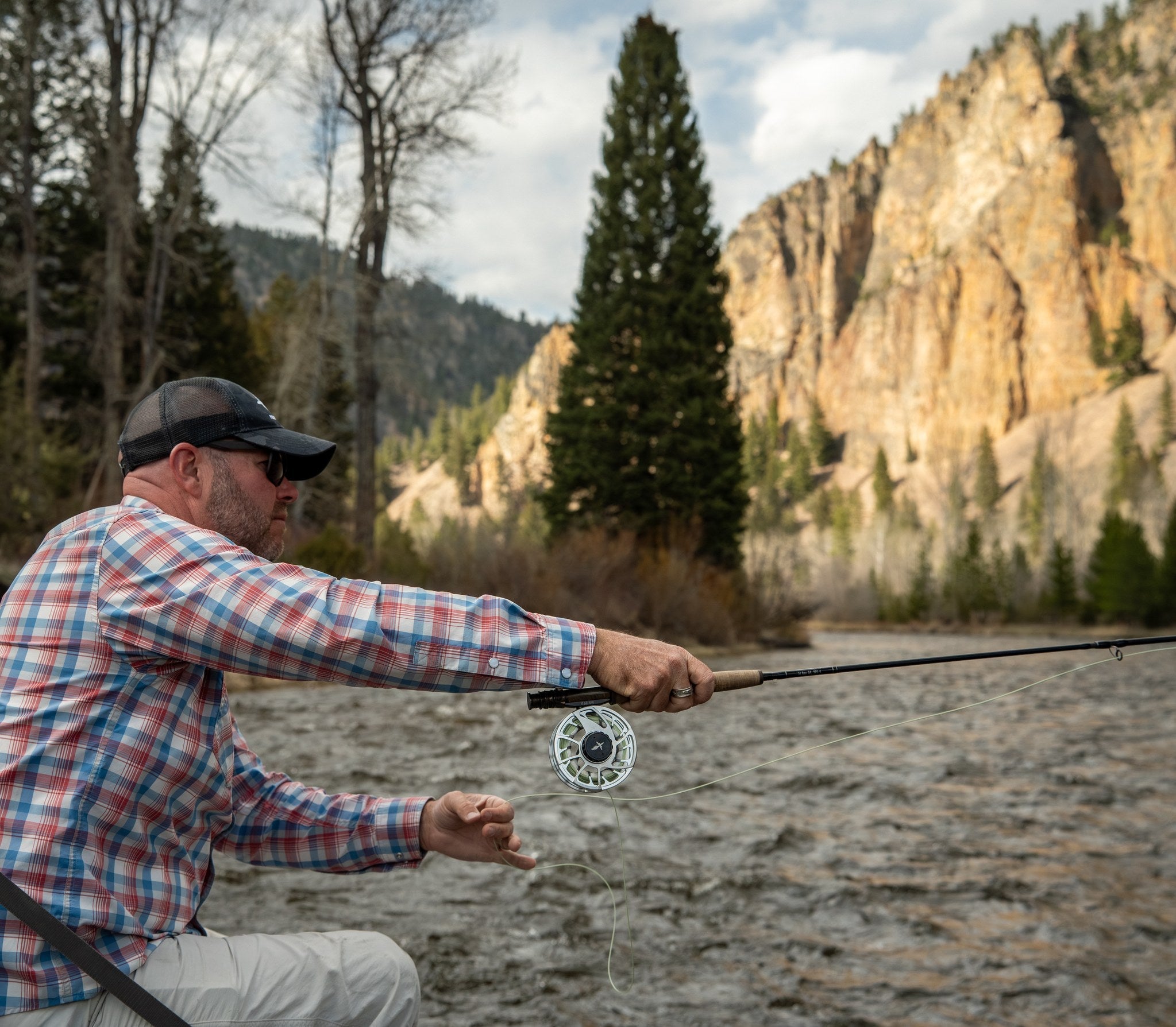 Angler fly casting on Rock Creek with a canyon cliff behind, Montana
